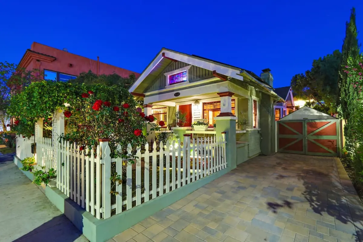 Beachwood Bungalow at twilight, a Craftsman cottage behind a white picket fence